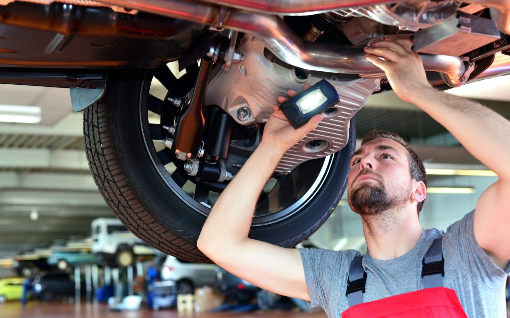 Mechaniker kontrolliert Abgasanlage eines Autos in der Werkstatt